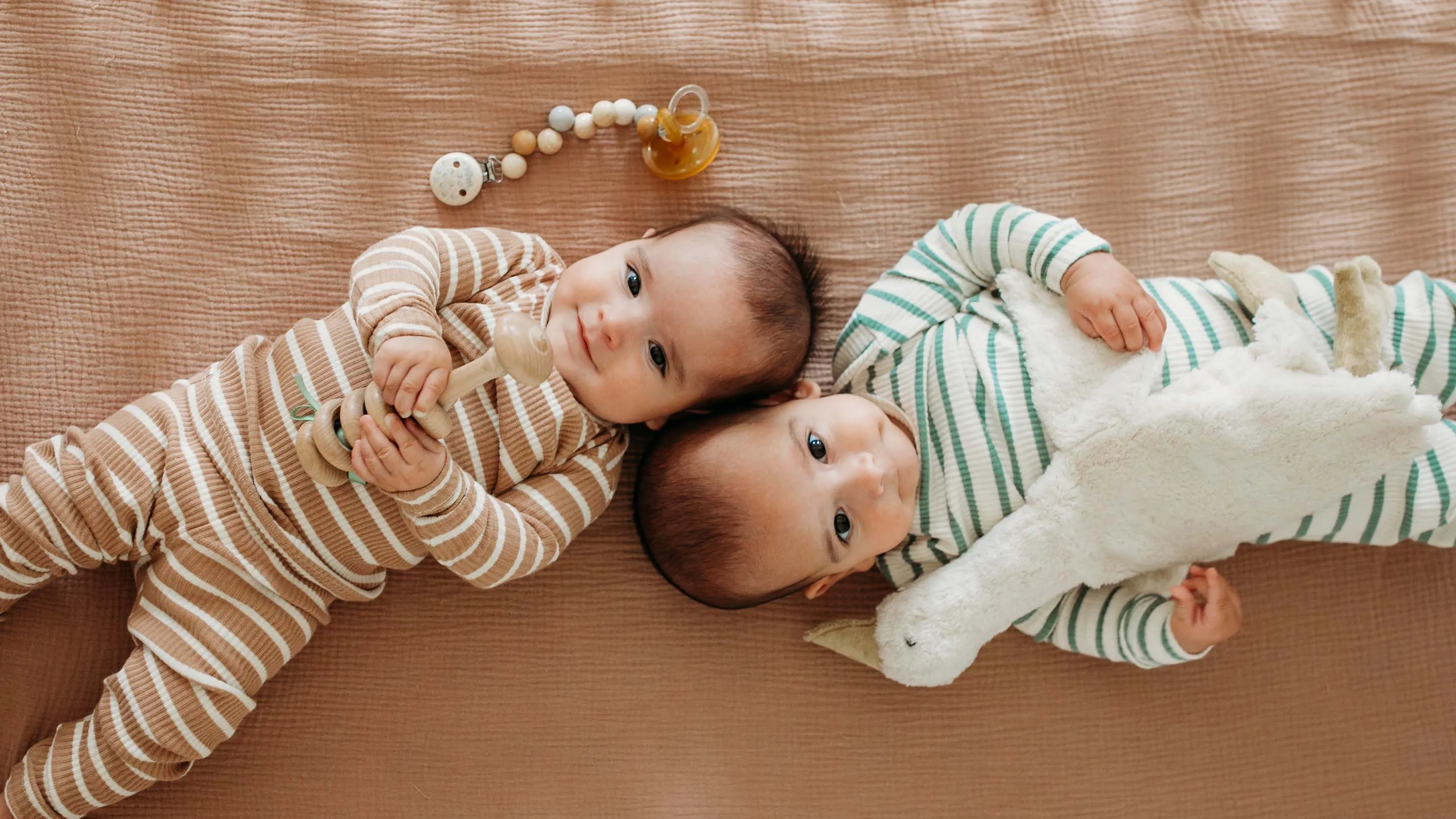 Two babies lying beside soft baby toys